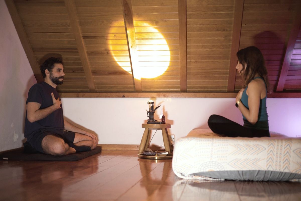João and a client sitting face to face, each with a hand on the chest, breathing together